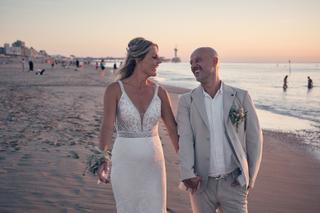 Bruidspaar Chris en Gerco loopt hand in hand op het strand van Scheveningen bij zonsondergang, trouwreportage - Trouwshoot St