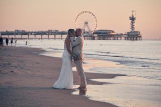 Bruidspaar Chris en Gerco kust op strand Scheveningen met pier en reuzenrad, romantische trouwfoto - Trouwshoot Stefan Segers