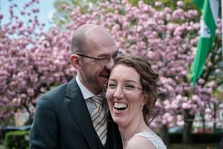 Bruidspaar Ilse en Robbert lacht samen voor bloeiende roze hortensia's, trouwreportage Boerderij Burgersdijk De Lier - Trouws