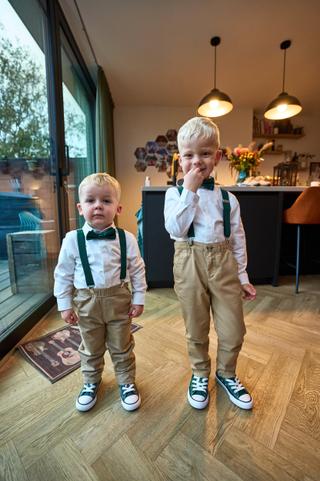 Twee bruidsjonkers in stijlvolle outfits met bretels en strikjes poseren in het moderne Breezze - Trouwshoot Stefan Segers