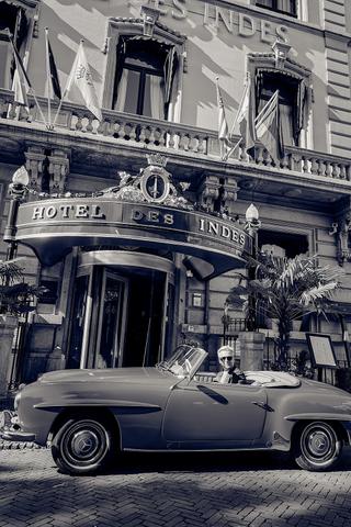Bruid Carlijn in vintage cabriolet voor Hotel Des Indes Den Haag, elegante trouwfoto met klassieke auto - Trouwshoot Stefan S