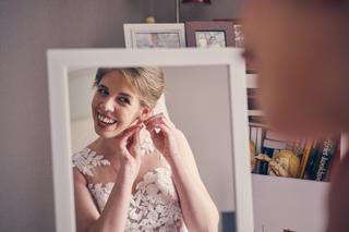 Bruid Marjolein in witte kanten trouwjurk lacht blij terwijl zij oorbellen aandoet, trouwreportage Clingendael Den Haag - Tro