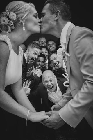 Bruidspaar Finley en Bas kust elkaar omgeven door lachende vrienden en familie - Trouwshoot Stefan Segers