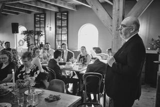 Vader van de bruid houdt speech tijdens het diner op Boerderij Burgersdijk. Gasten luisteren aandachtig in de rustieke zaal m