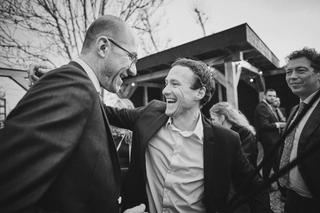 Bruidegom Robbert straalt van geluk terwijl gastheer hem feliciteert op Boerderij Burgersdijk - Trouwshoot Stefan Segers