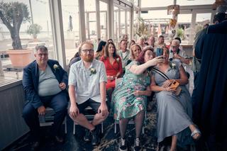 Gasten lachen en filmen met telefoon tijdens ceremonie op Beachhouse Kijkduin - Trouwshoot Stefan Segers