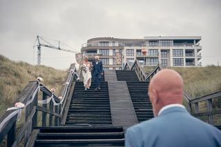 Bruid en bruidegom dalen trap af naar strand, gastheer ziet hen aankomen - Trouwshoot Stefan Segers