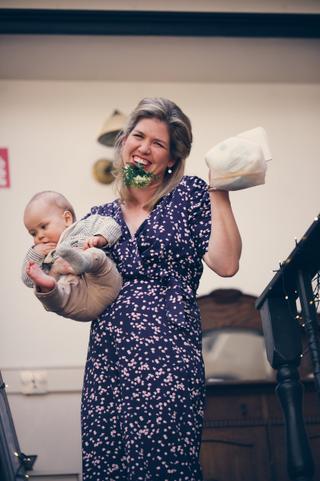 Bruid Marjolein met baby Hudson in haar armen, bloemenboeket glimlachend tijdens receptie Old Fashion Den Haag - Trouwshoot S