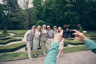 Tijdens de bruiloft van Yvo en Marjolein in Clingendael: familie poseren in formele outfits tussen de groene hagen, iemand ma