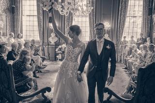 Yvo en Marjolein wandelen hand in hand door een elegante zaal met kristallen kroonluchter, omringd door gelukkige gasten - Tr