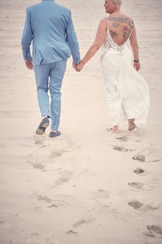 Bruidspaar Silvia en Patrick loopt hand in hand over het strand bij Beachhouse Kijkduin Den Haag, romantische trouwreportage