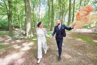 Bruidspaar Frank en Jennifer lopen hand in hand door bos met oranje rookbom, trouwreportage Clingendael Den Haag - Trouwshoot