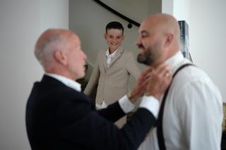 Jongeman in beige pak lacht met volwassenen in donkere pakken, trouwreportage Sodafabriek Schiedam - Trouwshoot Stefan Segers