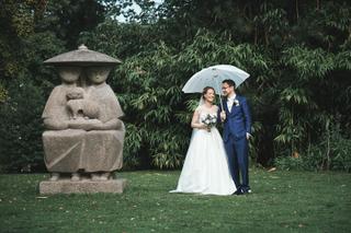 Bruidspaar onder paraplu op grasveld bij stenen sculptuur op kasteel Duivenvoorde - Trouwshoot Stefan Segers
