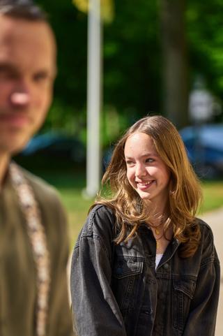 Elise lacht voluit in de zon op Beachclub Titus in Kijkduin, Erik op achtergrond - Trouwshoot Stefan Segers