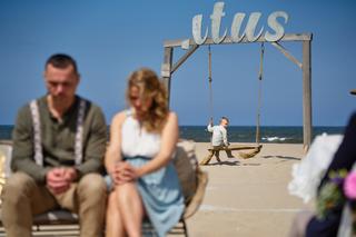 Kleine bruidsjonker speelt op de schommel bij beachclub Titus terwijl bruidspaar Elise en Erik toekijkt aan het strand - Trou