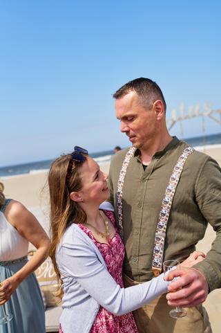 Elise en Erik genieten samen op het strand bij Beachclub Titus, het bruidspaar lachend in de zon met uitzicht op zee - Trouws