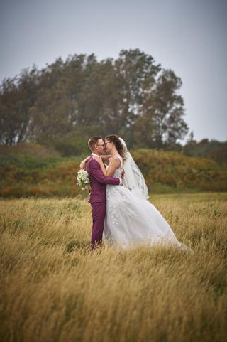 Emmely en Tom kussen in een golvend graanveld bij Villa Ockenburgh, bruid in wit kant met sluier - Trouwshoot Stefan Segers