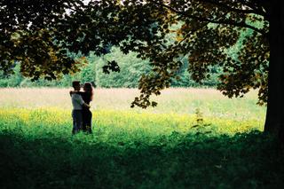 Verliefd stel omhelst elkaar onder oude boom met geel bloeiend veld op achtergrond in Zoetermeer, loveshoot — Trouwshoot