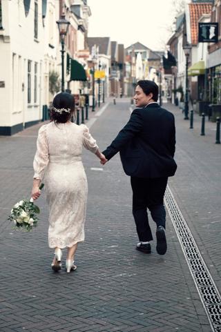 Bruidspaar hand in hand lopend door historische straat Zoetermeer, loveshoot met bruid in witte jurk — Trouwshoot Stefan