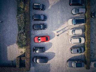 Luchtfoto van parkeerplaats met rode bruidauto tussen andere voertuigen, man met schaduw zichtbaar onderaan - Trouwshoot Stef