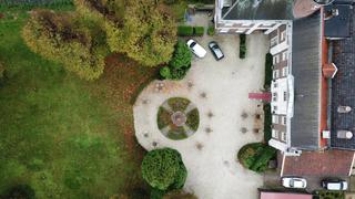 Luchtfoto van een elegant tuinfeest met rond terras, gezellige zithoeken en groene gazon omgeven door herfstkleuren - Trouwsh