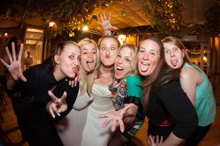 Bruid en bruidsmeisjes maken grappige gezichten op feestelijk verlichte trouwreceptie, vrolijke bruidsfotografie - Trouwshoot