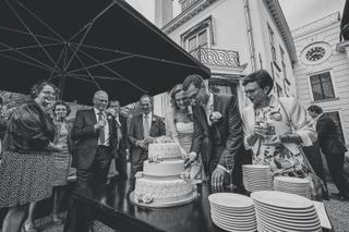 Bruidspaar snijdt taart tijdens receptie onder zwart parasol, familie en gasten kijken toe, elegant buitenfeest - Trouwshoot