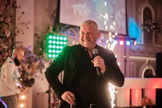 Man in zwart blazer spreekt in microfoon tijdens feestelijk bruidsfeest, festive sfeer met gekleurde verlichting - Trouwshoot