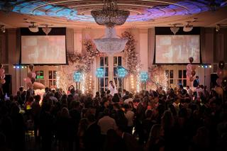 Bruidspaar danst op podium onder kristallen kroonluchter met roze bloemen, gasten feesten onder warm licht - Trouwshoot Stefa