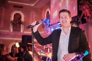 Bruidegom spreekt toespraak met microfoon op bruidsfeest, roze verlichte feestzaal, huwelijksreceptie - Trouwshoot Stefan Seg