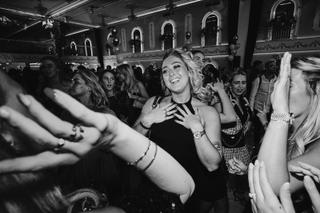 Bruid danst uitgelaten op bruidsfeest omringd door gasten in elegant zaalsetting - Trouwshoot Stefan Segers