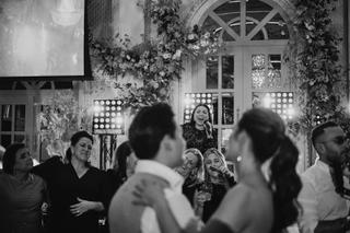 Bruidspaar danst uitgelaten op trouwfeest omringt door gasten, elegante zaal met bloemendecoratie en feestverlichting, vrolij