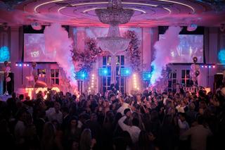 Bruidsfeest met dansend bruidspaar en gasten onder kristallen kroonluchter, roze neon sfeer met pyrotechnische effecten - Tro