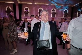 Bruidsgast geniet op trouwfeest in elegant paars verlicht zaal met drankje in hand, feestelijke trouwreportage - Trouwshoot S