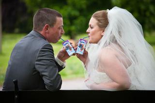 Bruidspaar drinkt speels uit SPA-flesjes in groene tuin, vrolijk trouwmoment, bruidsfotografie - Trouwshoot Stefan Segers