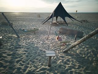 Mirjam en Jorg relaxen in hangmatten onder een zwarte strandtent met uitzicht op zee in Strandpaviljoen Brouw - Trouwshoot St