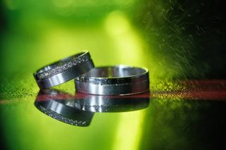 Trouwringen bruidspaar op groen gras, detail trouwreportage met diamanten ringen en reflectie - Trouwshoot Stefan Segers