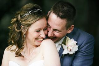 Bruidspaar lacht samen in intiem moment, bruid draagt tiara en parelketting, bruidegom met orchidee corsage - Trouwshoot Stef