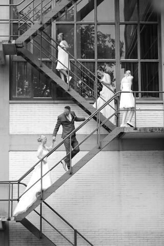 Bruidspaar loopt hand in hand op industriële trap, bruidjes in witte jurken, romantische trouwreportage - Trouwshoot Stefan S