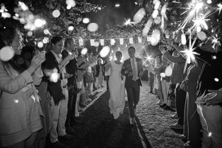 Bruidspaar loopt hand in hand door sparkler tunnel, gasten vieren bruiloft met gloeiende sterretjes 's avonds - Trouwshoot St