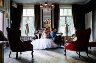 Bruidspaar Kirsten en Jouke zit samen op antieke bank in elegant zaaltje, trouwreportage Park Hugo de Vries Lunteren - Trouws