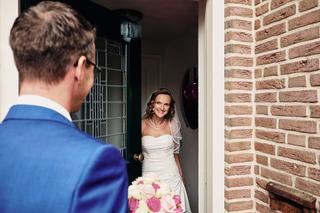 Bruid in witte jurk en sluier ontmoet bruidegom in blauw pak bij historische deur, eerste ontmoeting trouwreportage - Trouwsh
