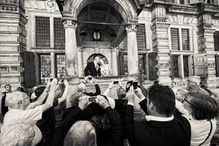 Bruidspaar kust op historisch balkon onder klassieke zuilen, gasten fotograferen moment - Trouwshoot Stefan Segers