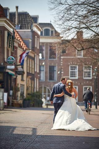 Bruidspaar loopt arm in arm door Hollandse straatsfeer met historische gevels, romantische trouwreportage - Trouwshoot Stefan