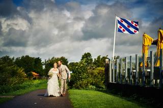 Bruidspaar loopt hand in hand over landweg met Friese vlag en groen landschap - Trouwshoot Stefan Segers