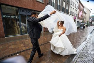 Bruidspaar Bellina en Cem in Venlo: bruid in wapperende tule onder regen op historisch plein bij stadhuis - Trouwshoot Stefan