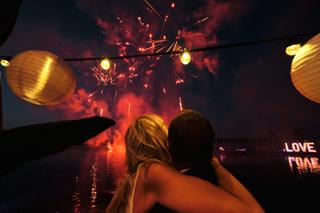 Bruidspaar Liad en Wilfried kijkt naar vuurwerk boven water, trouwfeest The Boathouse Kralingen Kralingse bos - Trouwshoot St