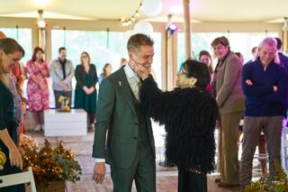 Bruidegom Glenn in groen pak wordt gefeliciteerd door een gast in zwarte faux fur op het feest van Karlijn en Glenn bij Breez