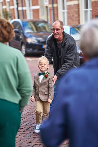 Bruidsjonker in pak met strik loopt lachend tussen gasten tijdens bruiloft Karlijn en Glenn - Trouwshoot Stefan Segers